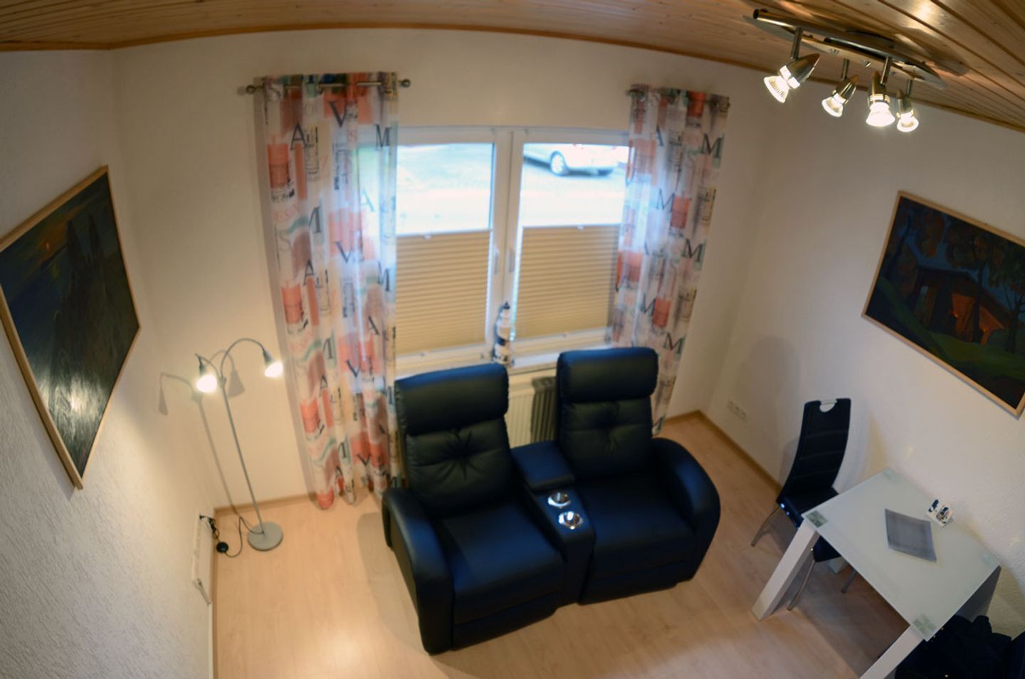 A room with two black leather chairs, a small table, a floor lamp, and a window with curtains.