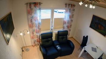 A room with two black leather chairs, a small table, a floor lamp, and a window with curtains.