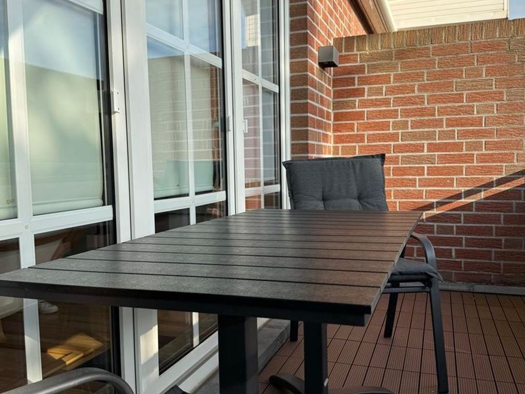 Un espace patio avec une table et des chaises en bois, un mur en briques et de grandes fenêtres.