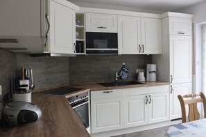 Una cocina moderna con armarios blancos, encimera de madera, horno empotrado y cafetera.