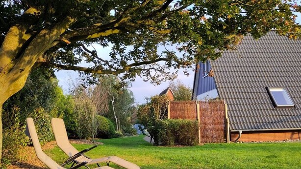 Une maison avec un toit en pente, une petite fenêtre et une cour verdoyante avec deux chaises longues.