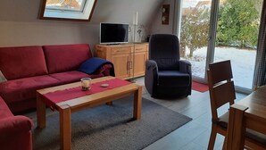 Un salon avec un canapé rouge, une table basse en bois, un fauteuil noir et un téléviseur posé sur un meuble en bois.