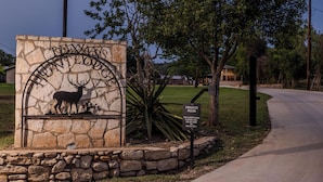 Un cartel que indica 'Texas Hunt Lodge', con una ilustración de un ciervo, un aviso de camino privado y un muro de piedra.