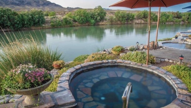 A hot tub surrounded by stone steps and plants, with a view of a calm lake and mountains in the background. - A retreat near Elephant Butte Lake with awesome views. Don’t miss out. Enjoy! (Elephant Butte)