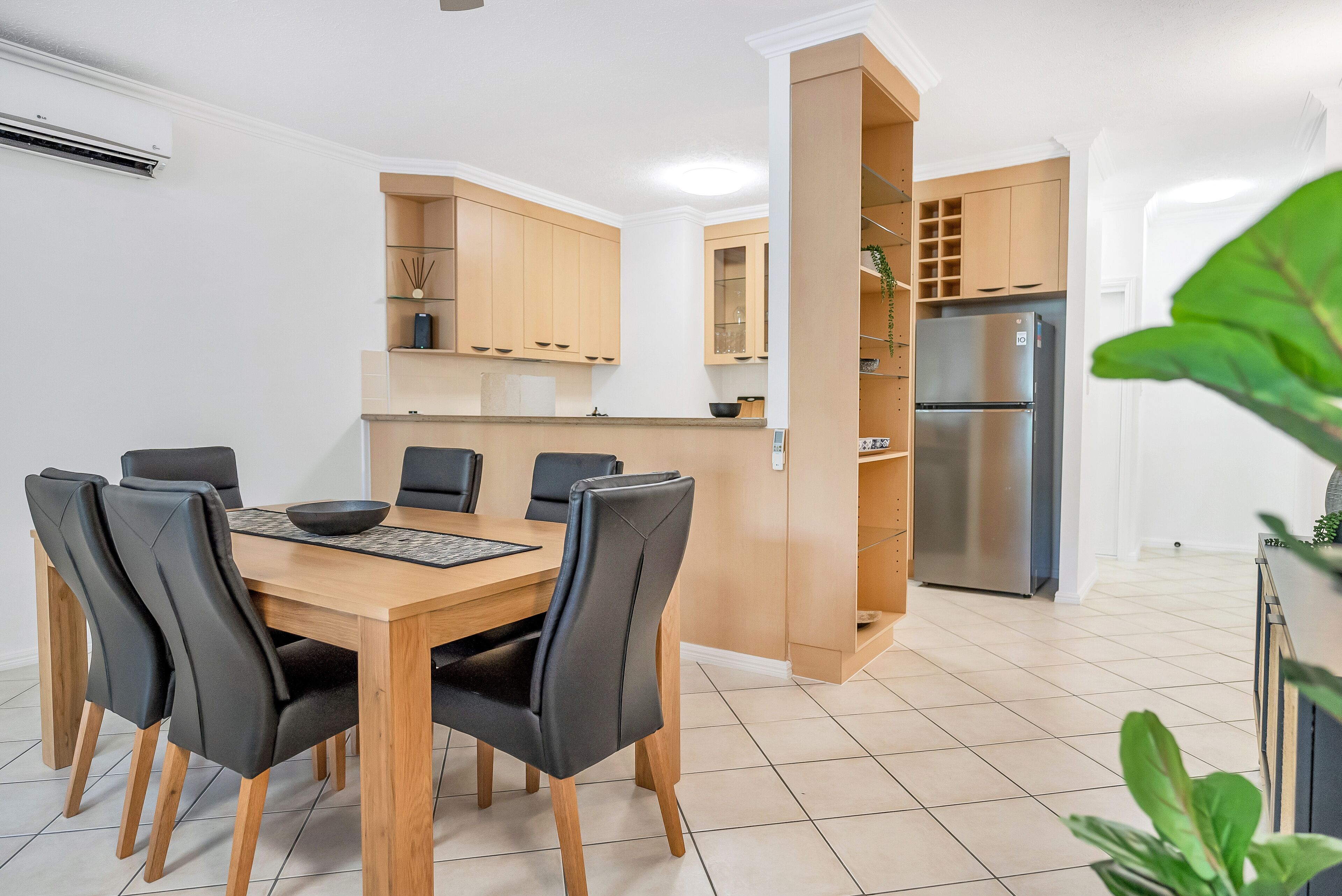 Een moderne keuken met houten kastjes, een roestvrijstalen koelkast en een eethoek met een houten tafel en zwarte stoelen.