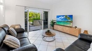 Ein modernes Wohnzimmer mit einem schwarzen Ledersofa, einem Holztisch und einem Fernseher auf einem Holzschrank.