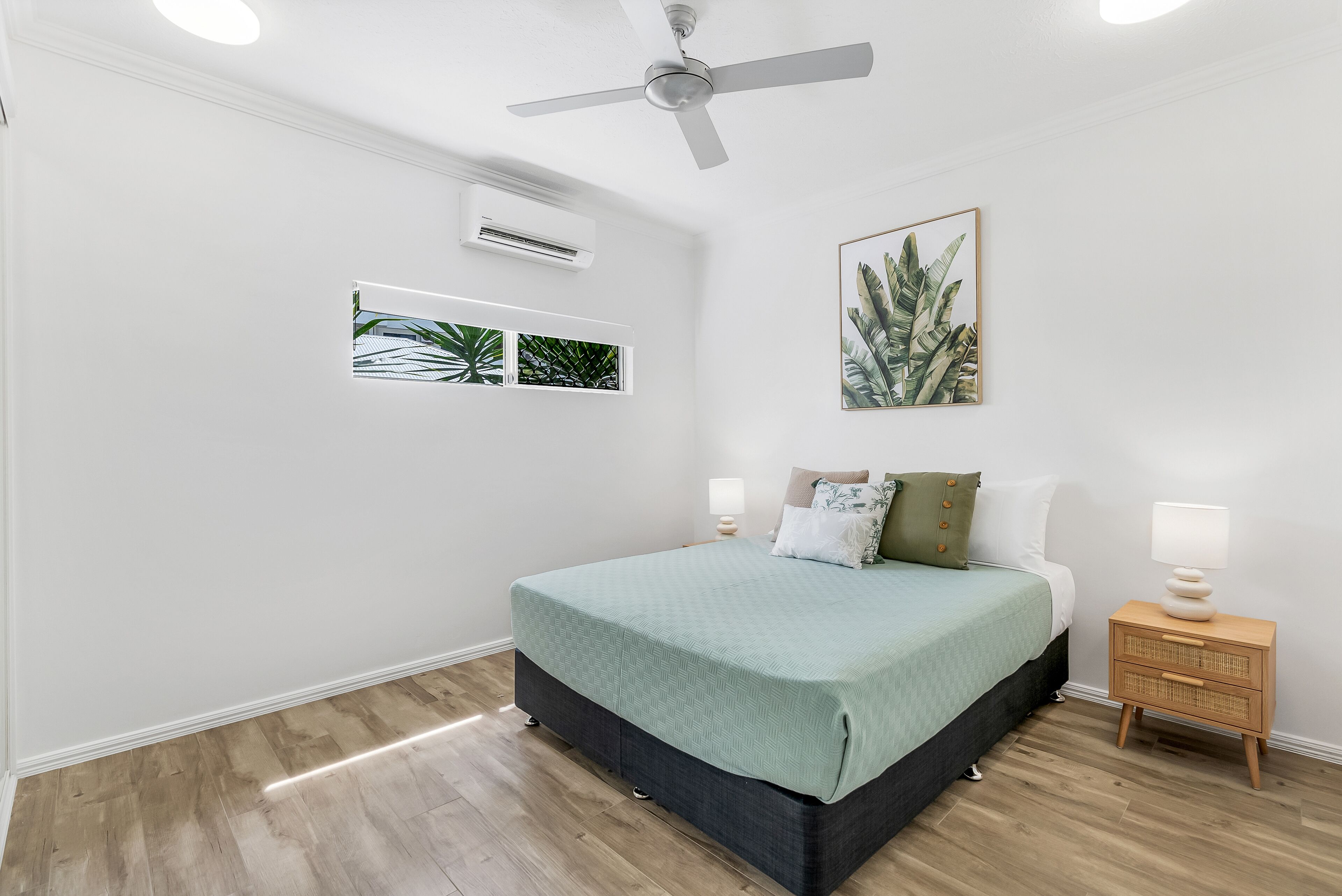 Un dormitorio con cama, mesitas de noche, ventilador de techo, aire acondicionado instalado en la pared y cuadros enmarcados.