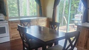 A dining area with a wooden table and chairs, a stove, and large windows with curtains. - Relax with the whole family at this peaceful place to stay. (Lead)
