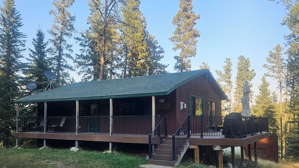 A rustic cabin with a green roof, a covered porch, and a deck with a grill. - Relax with the whole family at this peaceful place to stay. (Lead)