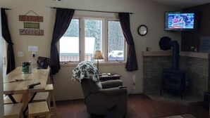 A cozy living room with a fireplace, a television mounted above it, and a window with curtains. - Relax with the whole family at this peaceful place to stay. (Lead)