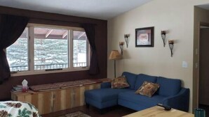 A cozy living room with a blue sofa, a wooden cabinet, and a window with a view of trees. - Relax with the whole family at this peaceful place to stay. (Lead)