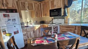A kitchen with wooden cabinets, a refrigerator, a microwave, a stove, and a dining table with chairs. - Relax with the whole family at this peaceful place to stay. (Lead)