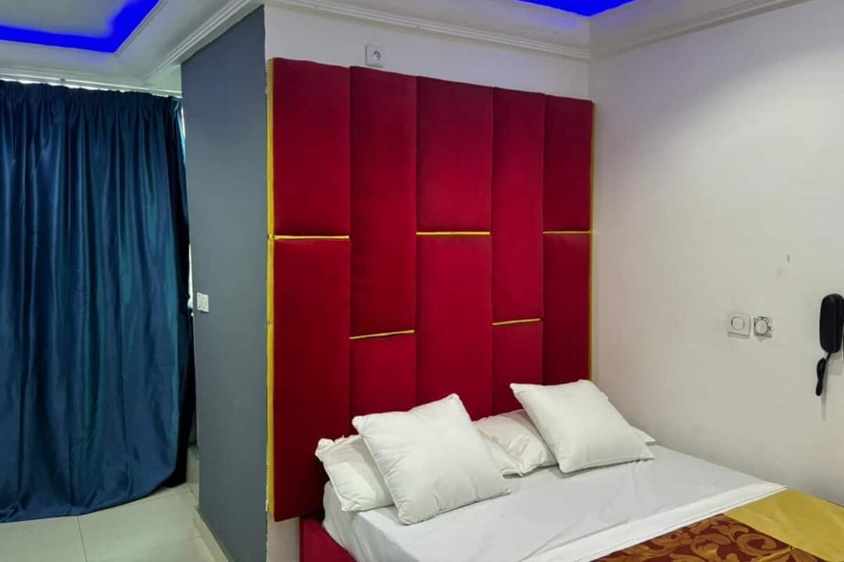 Un dormitorio con cabecera roja, ropa de cama blanca y cortina azul.