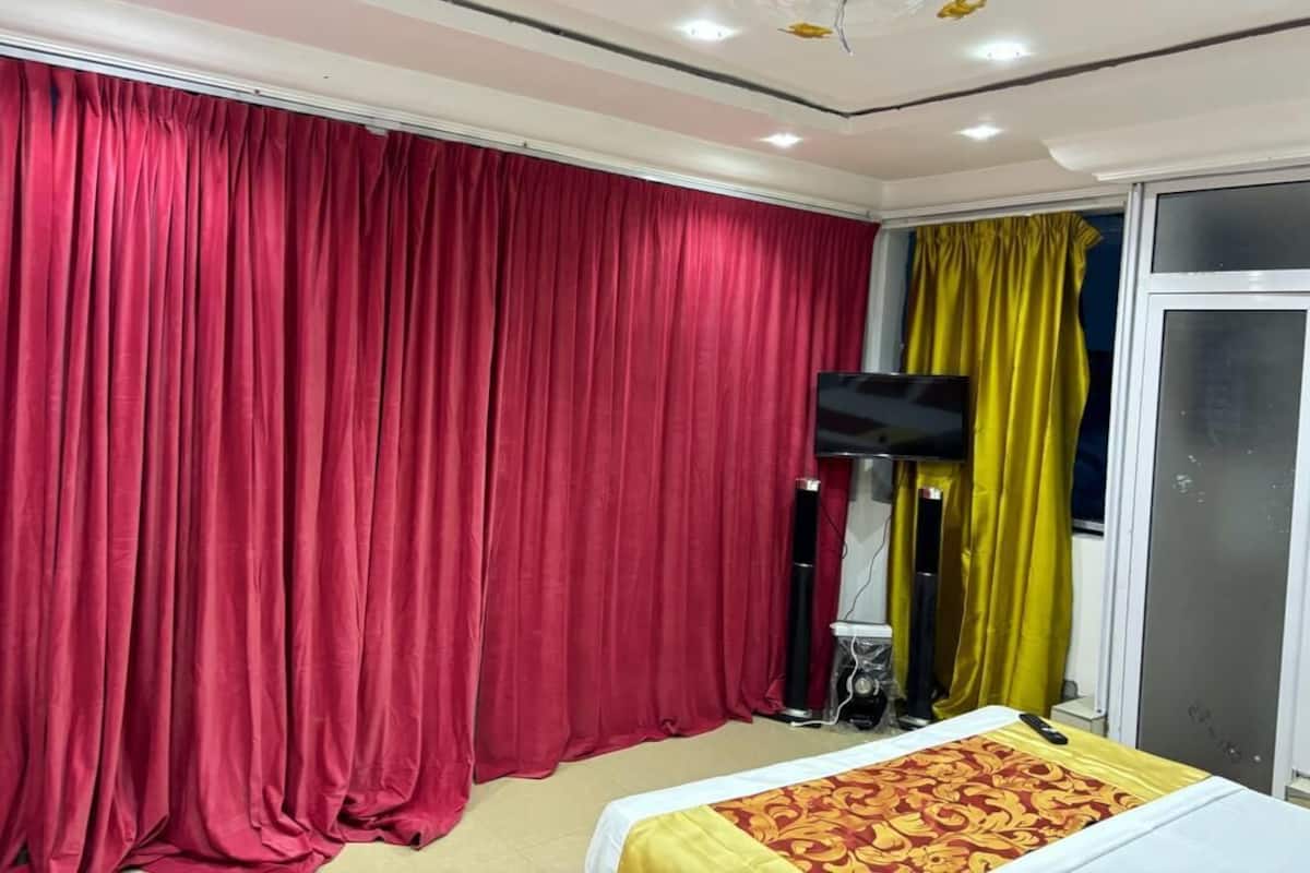 Una habitación con una cama, televisión y ventana con cortinas.