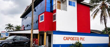A building with a red, white, and blue facade, a motorcycle parked in front, and a car parked to the left.