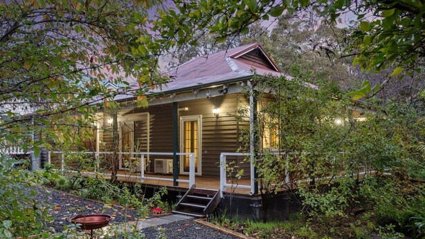 Een houten huis met veranda, omgeven door weelderige begroeiing.