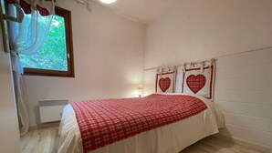 A bedroom with a bed, a window with curtains, a radiator, and heart-shaped decorations on the wall. - Wonderful apt 4/6 ppl, mountain view (Les Deux Alpes)