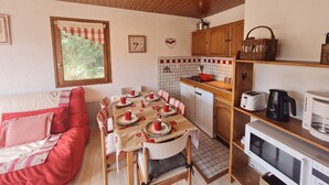A cozy kitchen with wooden cabinets, a dining table set for four, and a window with a view of greenery. - Wonderful apt 4/6 ppl, mountain view (Les Deux Alpes)