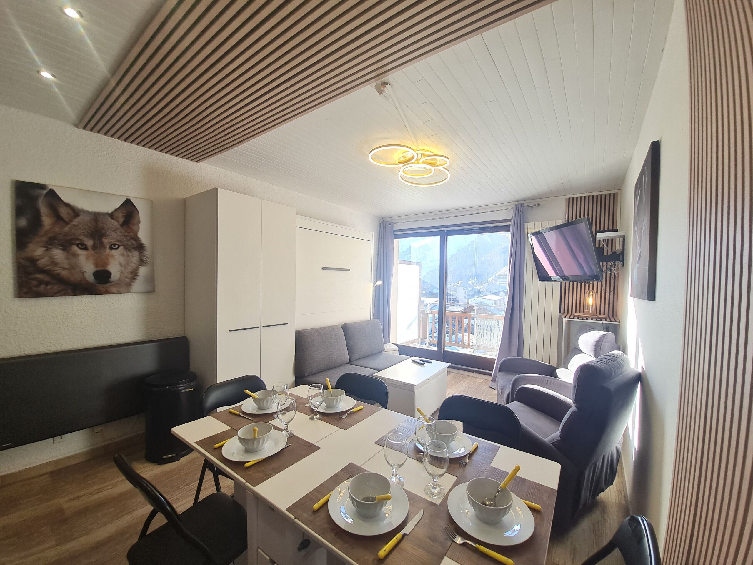 Un coin repas avec une table dressée pour quatre personnes, un canapé et un téléviseur fixé au mur.