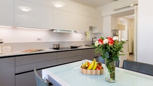 A modern kitchen with white cabinets, a glass-top dining table, and a fruit bowl.