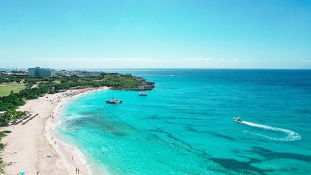 Een kuststrand met helder turquoise water, een zandstrand en enkele boten.