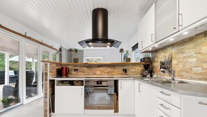 Una cocina moderna con armarios blancos, salpicadero de piedra y horno empotrado.