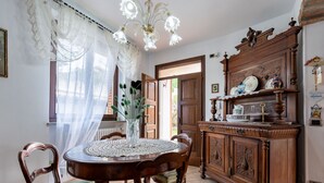Ein Essbereich mit einem runden Tisch, Stühlen, einer Blumenvase, einer Chandelüster und einer Holzkommode mit Dekorationen.