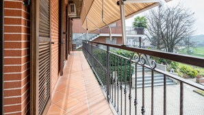 Ein überdachter Balkon mit Fliesenboden, Metallgeländer und Blick auf eine Wohngegend mit Häusern und Bäumen.