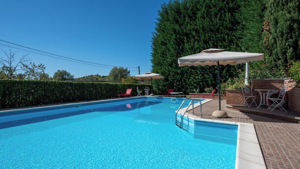 Ein rechteckiger Swimmingpool mit klarem, blauem Wasser, umgeben von einer Ziegelterrasse mit Liegestühlen und Sonnenschirmen.