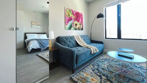A modern bedroom with a blue sofa, a bed, a small table, and a large window.