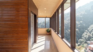 Un pasillo con paneles de madera, una planta en maceta y grandes ventanales que ofrecen vistas a una ladera boscosa.