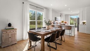 Et moderne køkken med hvide skabe, en central ø og et spiseområde med et træbord og stole.