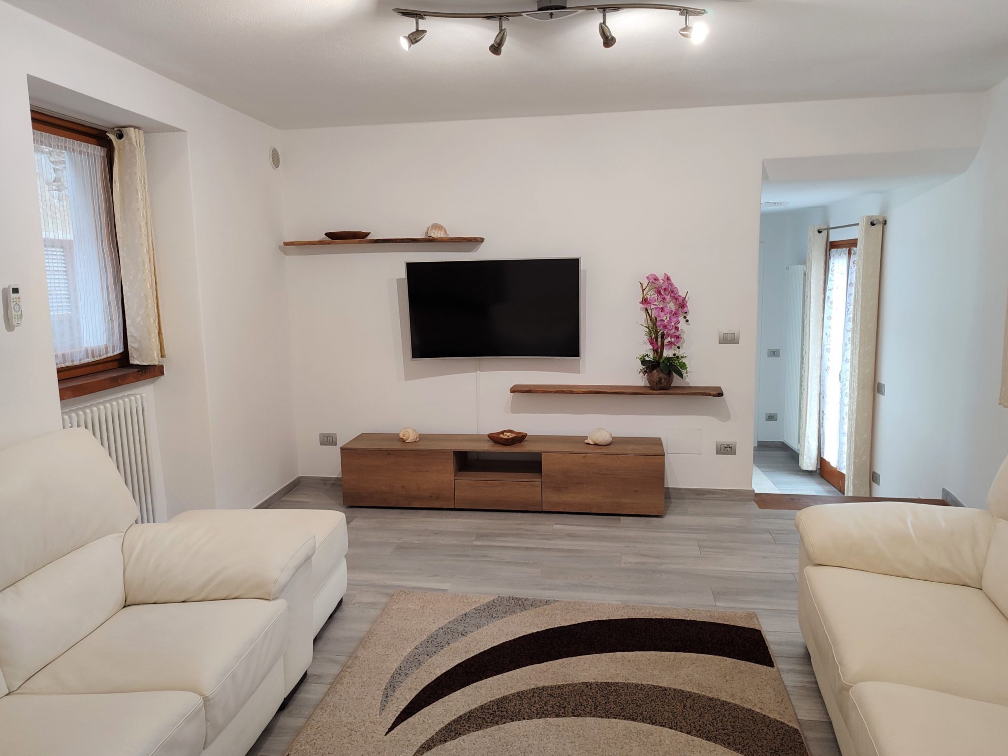 Un salon moderne avec un téléviseur à écran plat fixé au mur, un meuble de rangement en bois en dessous et deux canapés de couleur crème.