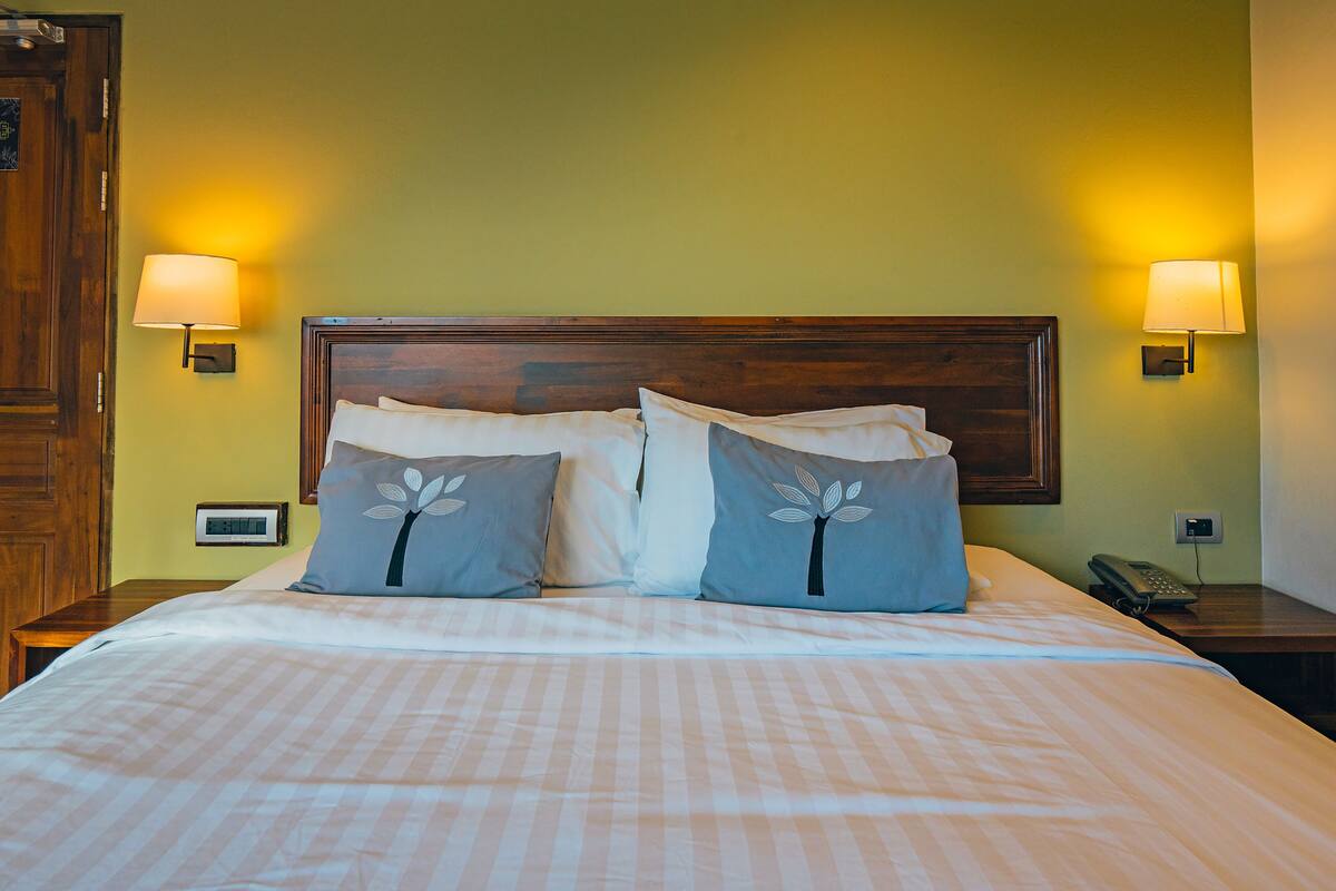 Una cama bien hecha con cabecera de madera, dos lámparas de noche y una mesita de noche con un teléfono.