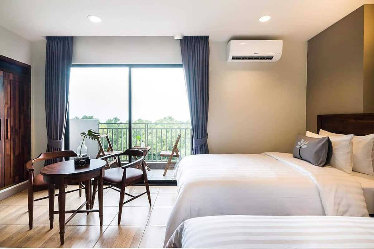 Una habitación de hotel con balcón, una cama, una mesa y sillas, y un equipo de aire acondicionado.