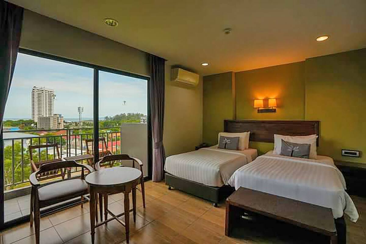 Habitación de hotel con dos camas, un balcón con mesa y sillas, y vistas a la ciudad.
