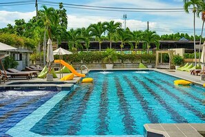 Una piscina con tobogán, sillas de descanso y sombrillas.