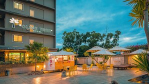 The Olive Tree Hotel with outdoor seating, palm trees, and a clear sky. - Olive Tree Hotel (Sattahip)