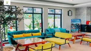 A modern lounge area with teal and yellow furniture, large windows, and a clock on the wall. - Olive Tree Hotel (Sattahip)