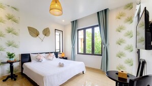 A hotel room with a bed, a desk, a chair, a TV, and a window with curtains. - Luna Verde Hotel Hoi An (Da Nang)