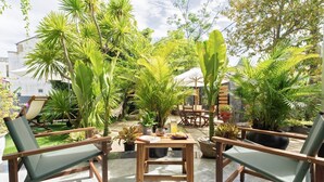A patio area with wooden furniture, potted plants, and a table with a book and a glass. - Luna Verde Hotel Hoi An (Da Nang)