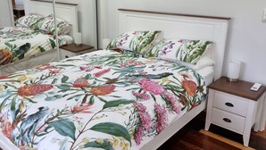 A bedroom with a bed, a nightstand, a mirror, and an air conditioning unit. - Yungaburra Whitehouse 
Walking distance to village (100 metres)
2 ensuites (Yungaburra)