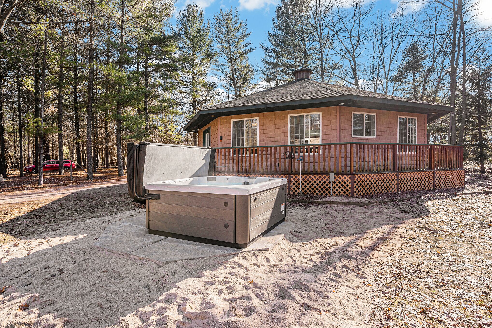A hot tub in a sandy area with a wooden deck and a house in the background.