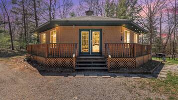 A wooden cabin with a front door, windows, and a deck.