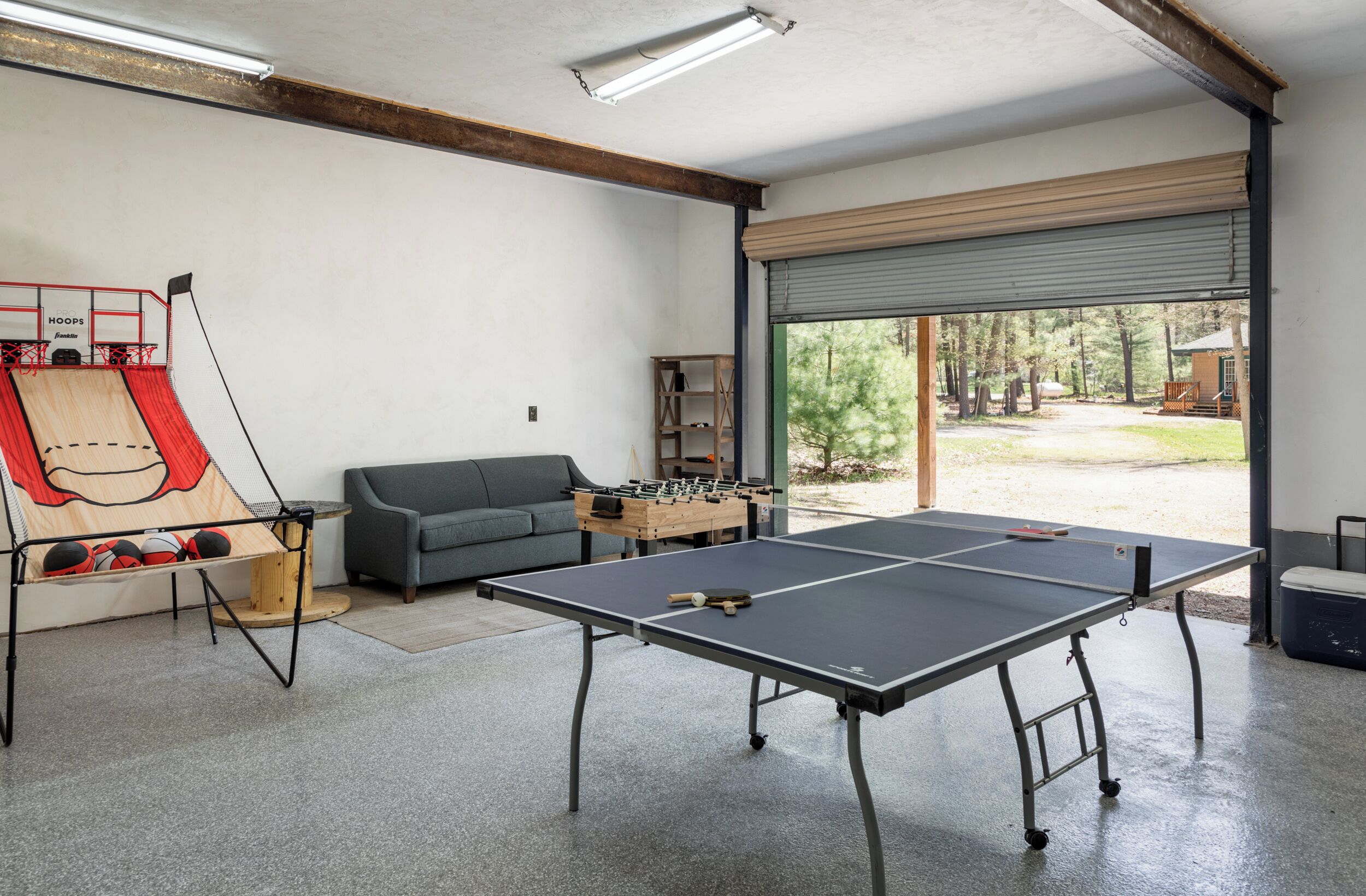 Une pièce équipée de deux tables de ping-pong, d’un baby-foot, d’un canapé et d’une grande fenêtre donnant sur la verdure.
