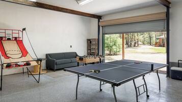 Une pièce équipée de deux tables de ping-pong, d’un baby-foot, d’un canapé et d’une grande fenêtre donnant sur la verdure.