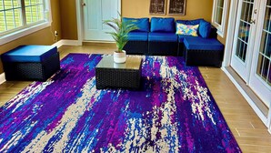 A living room with a large purple and blue rug, a ceiling fan, and a sofa with blue cushions.