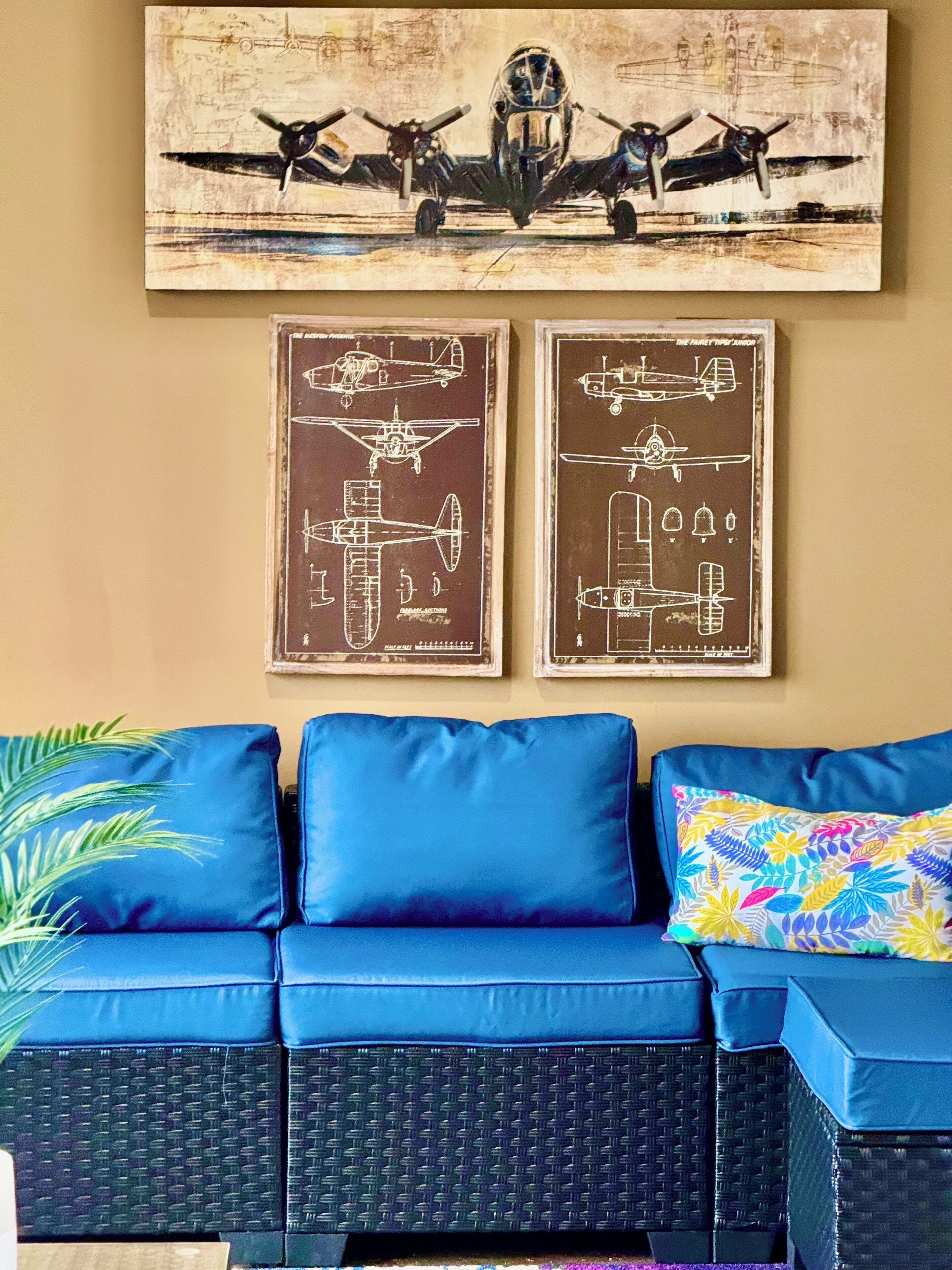 Un salon avec un ensemble de meubles bleus, dont un canapé, un tableau représentant un avion accroché au mur, et deux schémas d’avions encadrés.