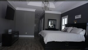A bedroom with a dark wood floor, a large bed with white bedding, a dark wooden headboard, a bedside table, a mirror, and a ceiling light fixture.