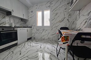 Una cocina con armarios blancos, salpicadero de mármol, una ventana y una mesa con mantel decorado con motivos de comida.